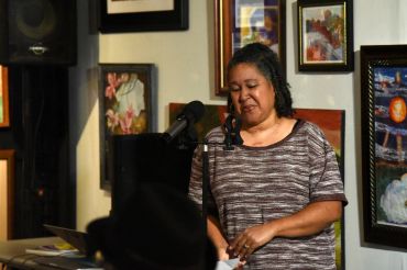Woman speaking at a microphone in an art gallery.