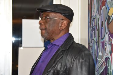 Older man wearing a leather jacket and cap looking sideways.