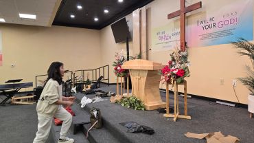 Person preparing a church stage with floral arrangements and decorations.