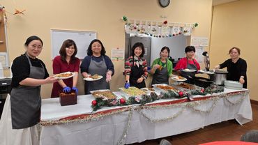 Seven women smiling behind a decorated holiday buffet table.