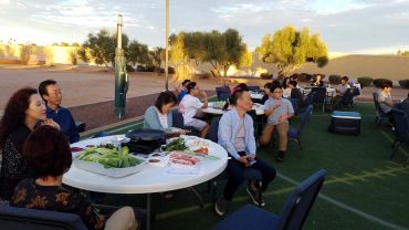 People gathered outdoors around tables enjoying a meal and conversation at sunset.