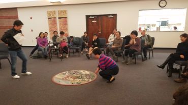 A group playing a traditional game indoors with a circular board on the floor.