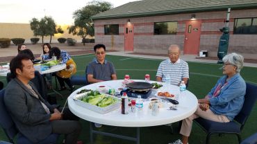 A group of people sitting around a white round table outdoors with food and drinks.