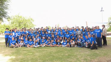 Large group photo of people wearing matching blue shirts outdoors.