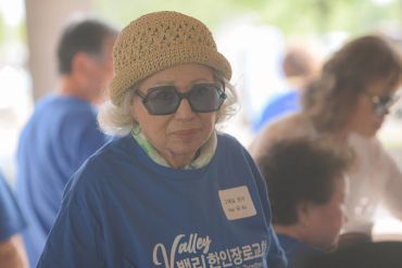 Elderly woman in a hat and sunglasses at a community event.