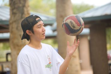 Young man in a cap spinning a volleyball on his finger outdoors.