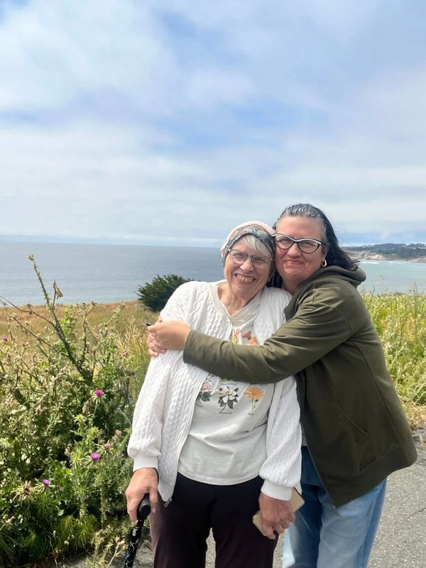 Two women hugging near the ocean with smiles.