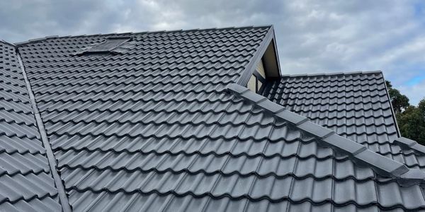 A house roof with dark gray metal tiles under a cloudy sky.