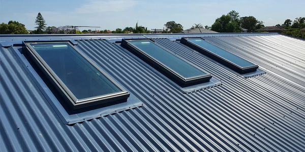 Three rectangular skylights on a blue corrugated metal roof under a clear sky.