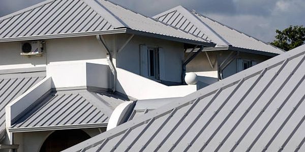 Modern house rooftops with gray metal roofing under a cloudy sky.