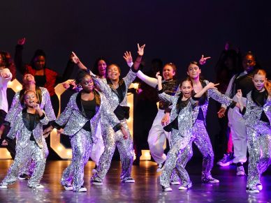 Group of dancers in sparkly silver costumes performing on stage.