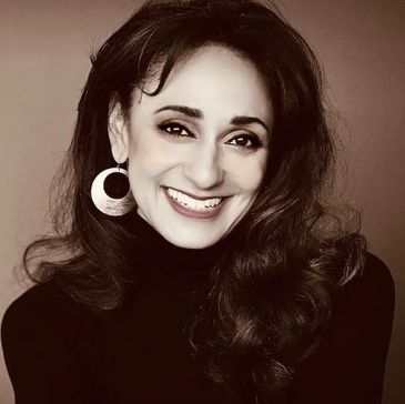 Smiling woman with long hair and large hoop earrings.