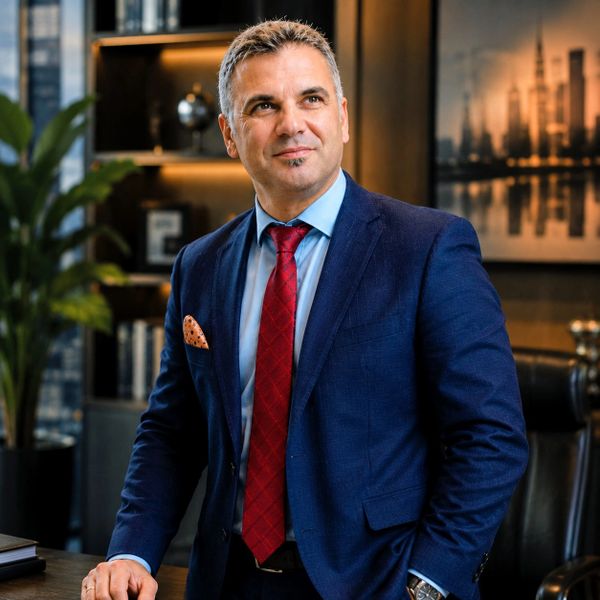 Confident businessman in a blue suit and red tie standing in a modern office.