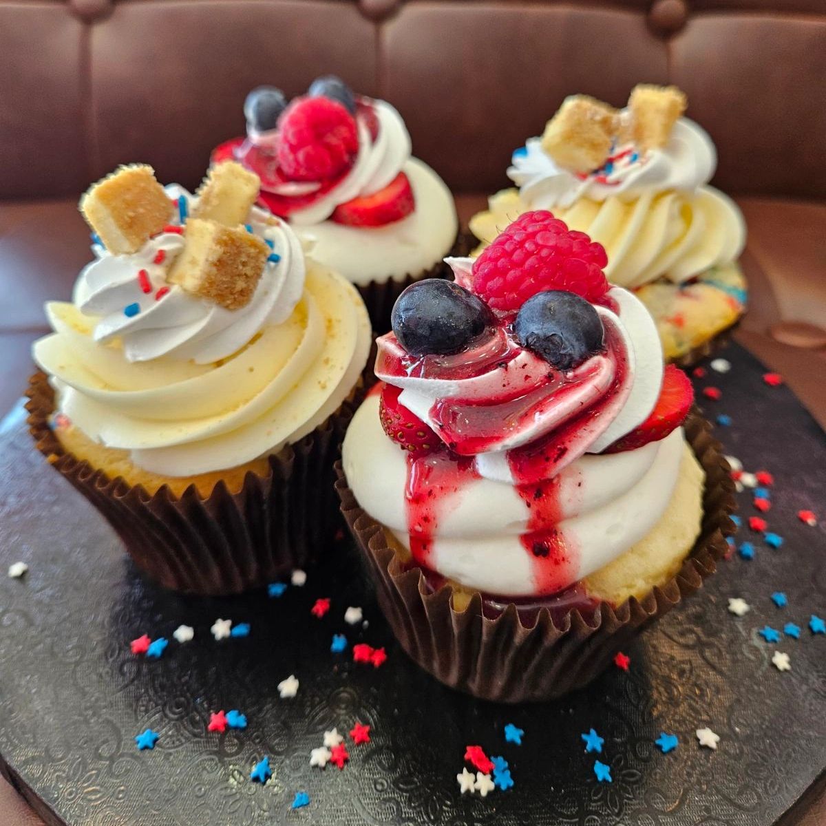 Four decorated cupcakes with berries and cream.