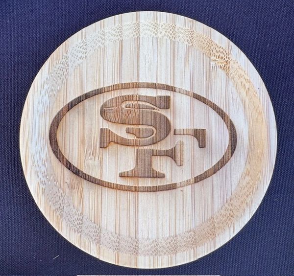 Wooden coaster with engraved SF logo on dark fabric background.