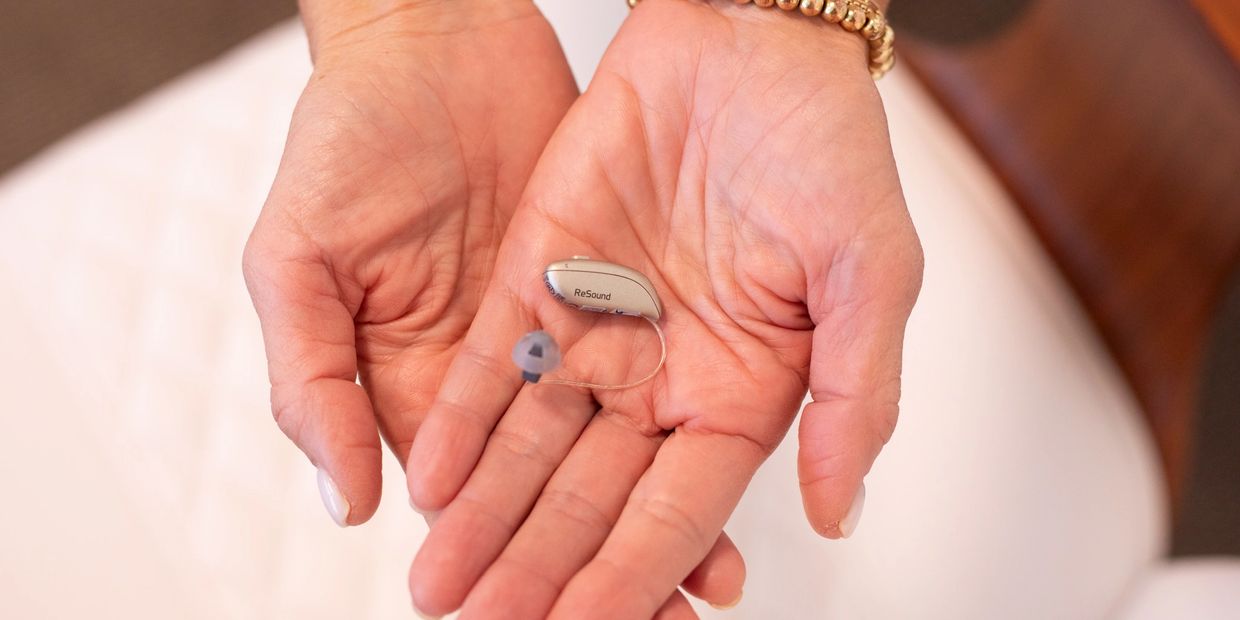 Hands holding a small hearing aid device labeled ReSound.