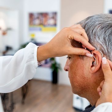 A hearing aid is being fitted, programmed, adjusted, repaired, and fitted on an older man.