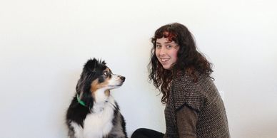 A woman sitting next to a black and white dog against a plain background.