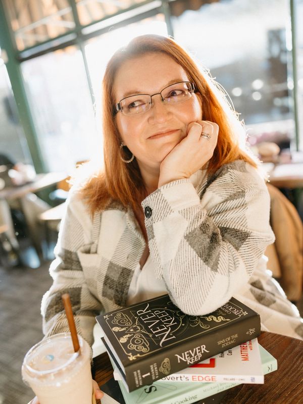 Smiling woman in glasses with books and iced drink at a cafe.
