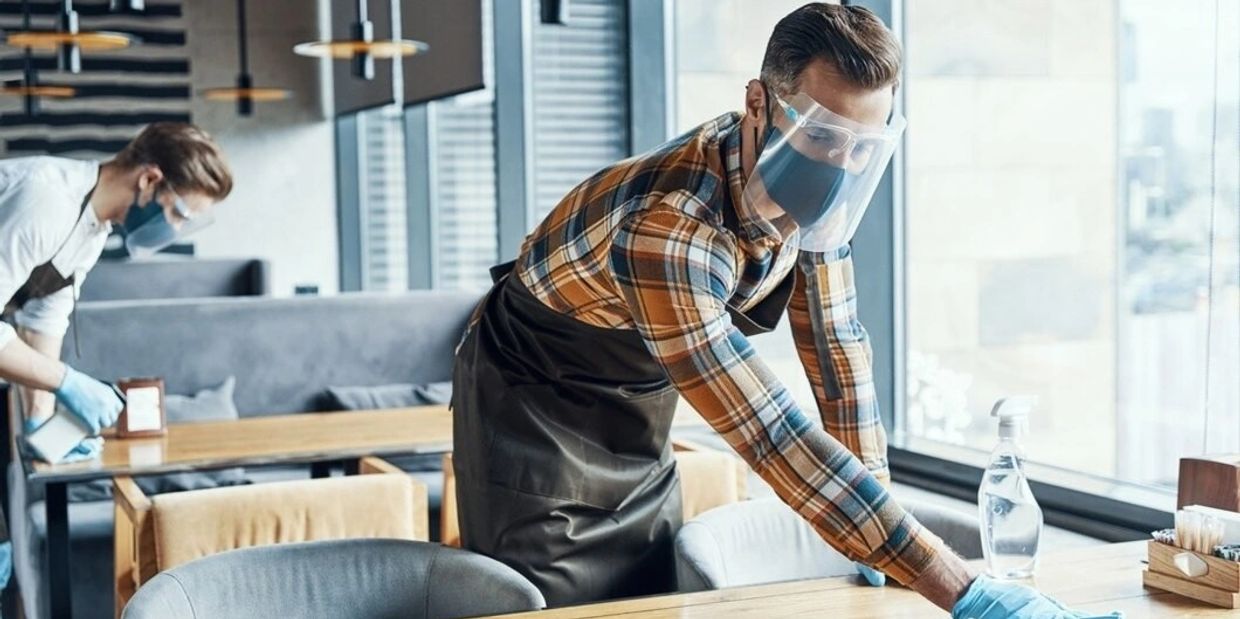 Workers cleaning tables wearing protective masks and gloves.
