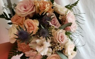 Cascading bridal bouquet of blush, white, peach, and pink flowers accented with blue and foliage