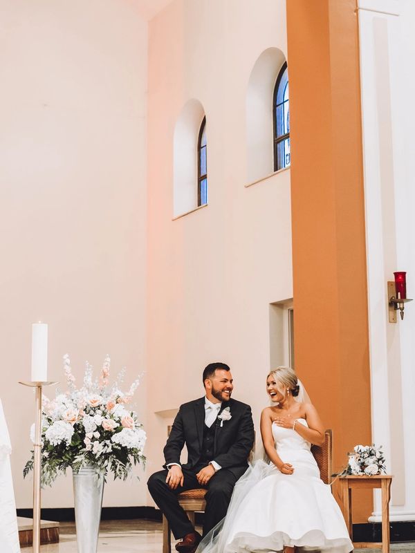 Bride and Groom sitting on the alter at church with alter arrangement and bridal bouquet 