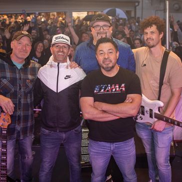 A band posing for a photo with an enthusiastic crowd behind them.
