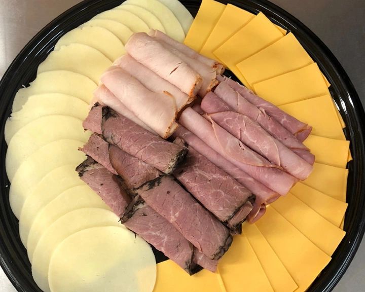 Provolone & yellow American cheese sitting on a circular serving tray with lunch meats rolled on top