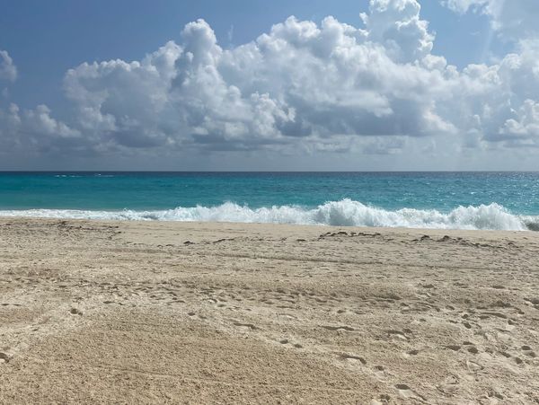 Sunny beach with turquoise waves and fluffy clouds.