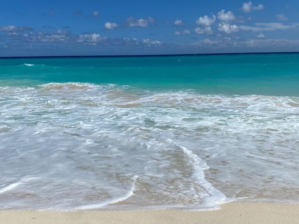 Clear blue ocean waves gently washing onto a sandy beach under a bright sky.