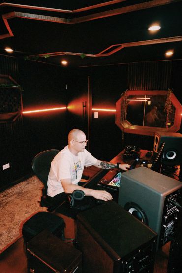 Man working in a dark music studio with glowing lights.