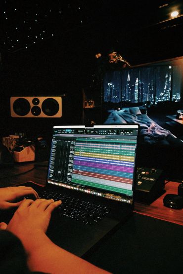 Person editing music on a laptop in a dark room.