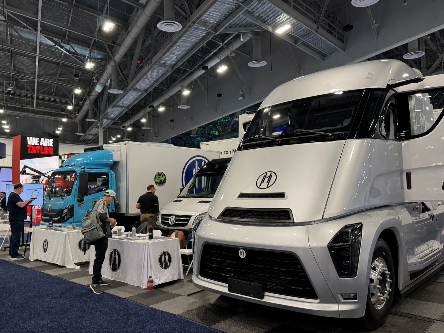 Electric trucks showcased at an indoor automotive expo with people exploring the displays.
