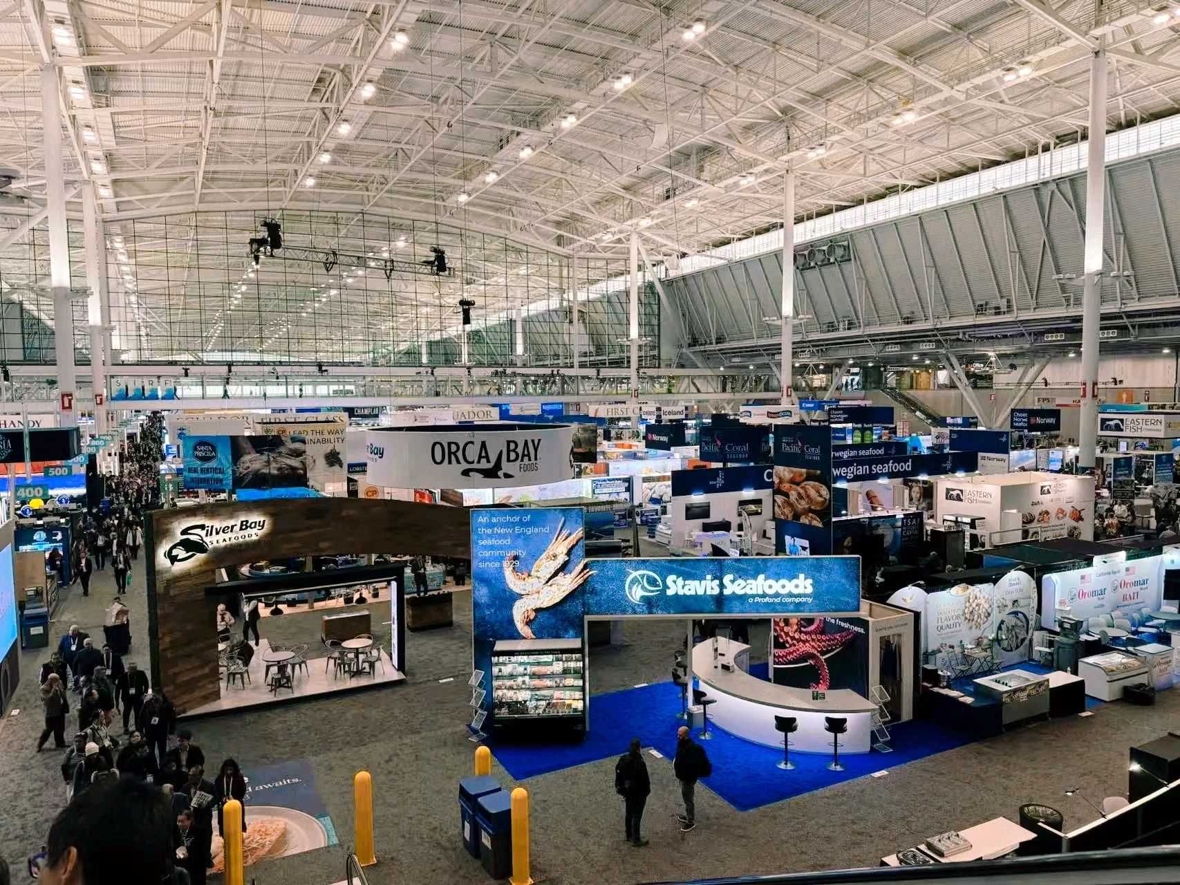 A bustling seafood trade show with various company booths and attendees.