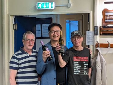 Three men smiling, holding wine bottles indoors.