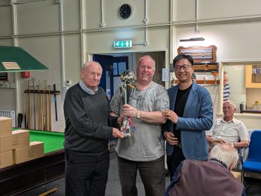 Three men posing with a trophy in a game room.
