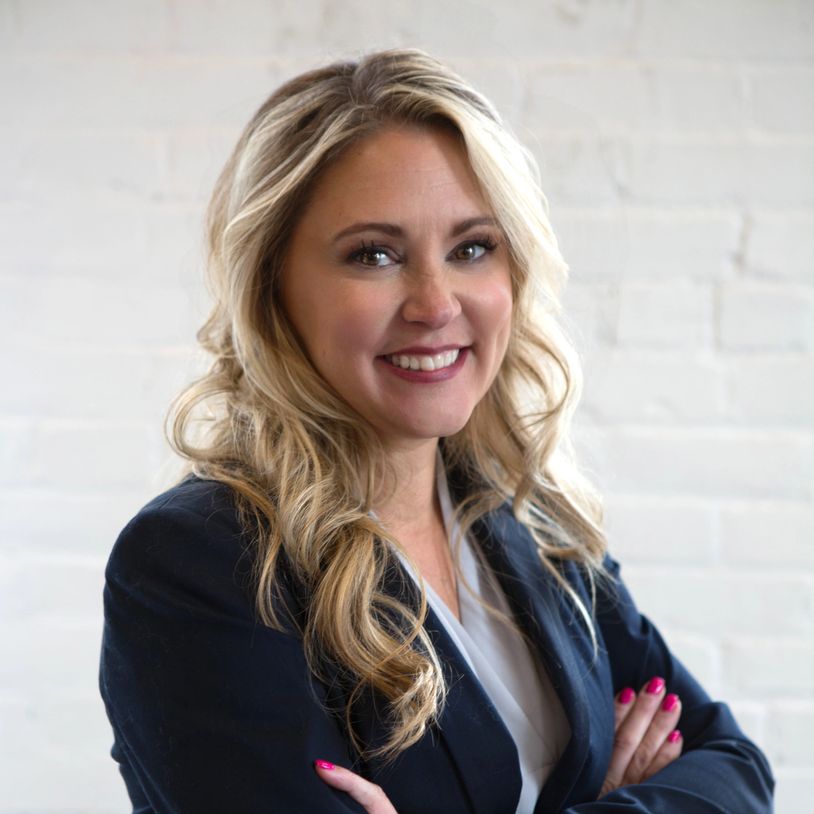 Professional woman with blonde hair smiling confidently in business attire.