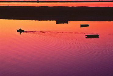 Boat on calm water at sunset with vibrant orange and purple hues.