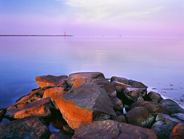 Rocks leading into calm sea with distant lighthouse.