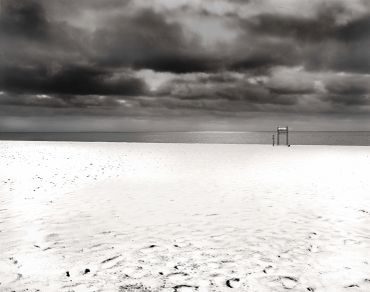 Bleak beach scene with dark clouds and empty lifeguard chair.