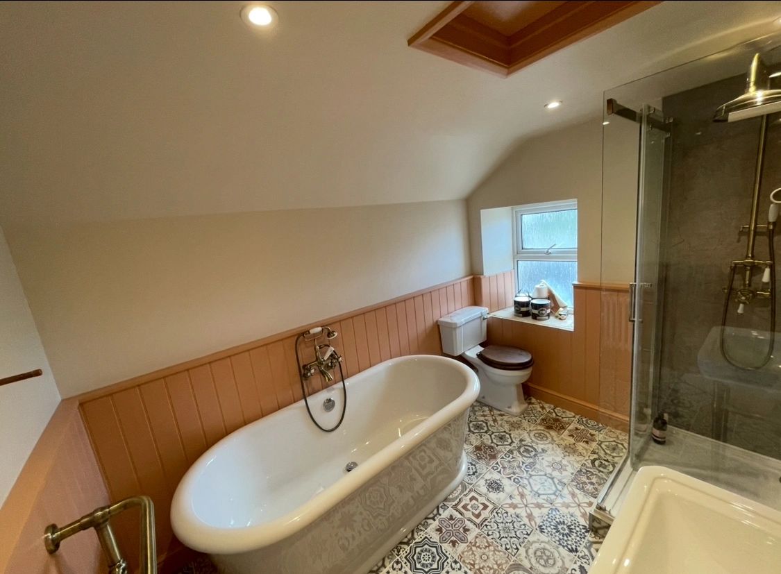 A Bathroom with freestanding bath and victorian motif on floor tiles, and pinkish orange panelling