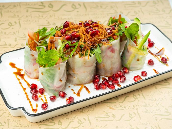 Fresh vegetable spring rolls garnished with pomegranate seeds and drizzled sauce.