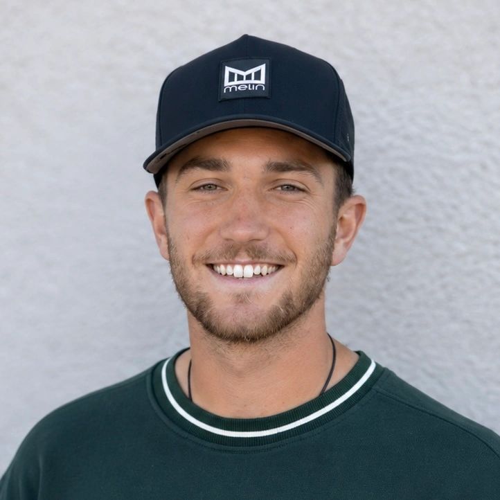 Smiling young man wearing a black cap and green sweatshirt.