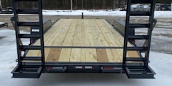 Empty flatbed trailer with ramps on snowy ground.