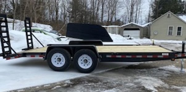 Flatbed trailer with ramps parked on snowy ground near a house.