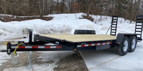 Flatbed trailer with dual axles parked on a snowy gravel lot.