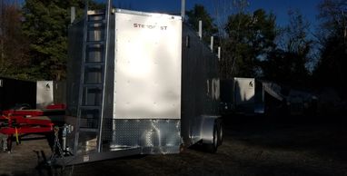 A silver trailer with a ladder on the front parked outdoors.