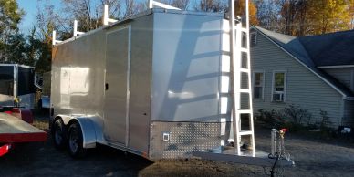Silver enclosed trailer with ladder parked near a house.