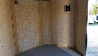 Empty wooden shed corner with plywood walls and gray floor.