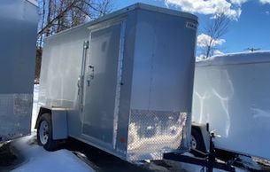 Silver enclosed trailer parked on snow-covered ground under blue sky.